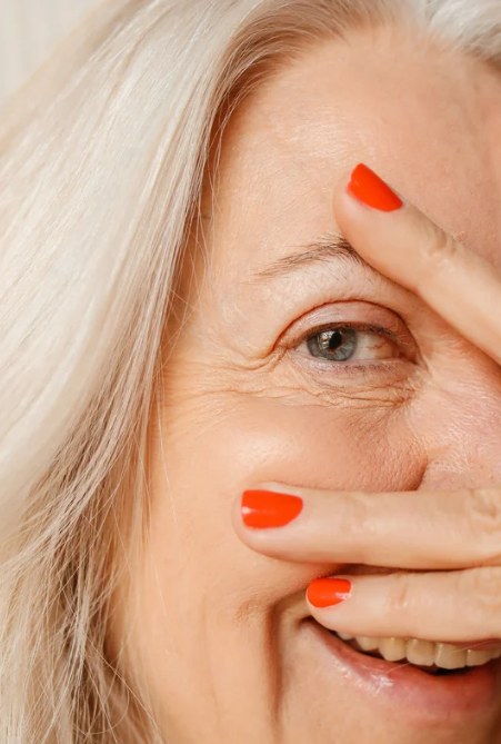 Joyful client with bright red nails peeking through her fingers